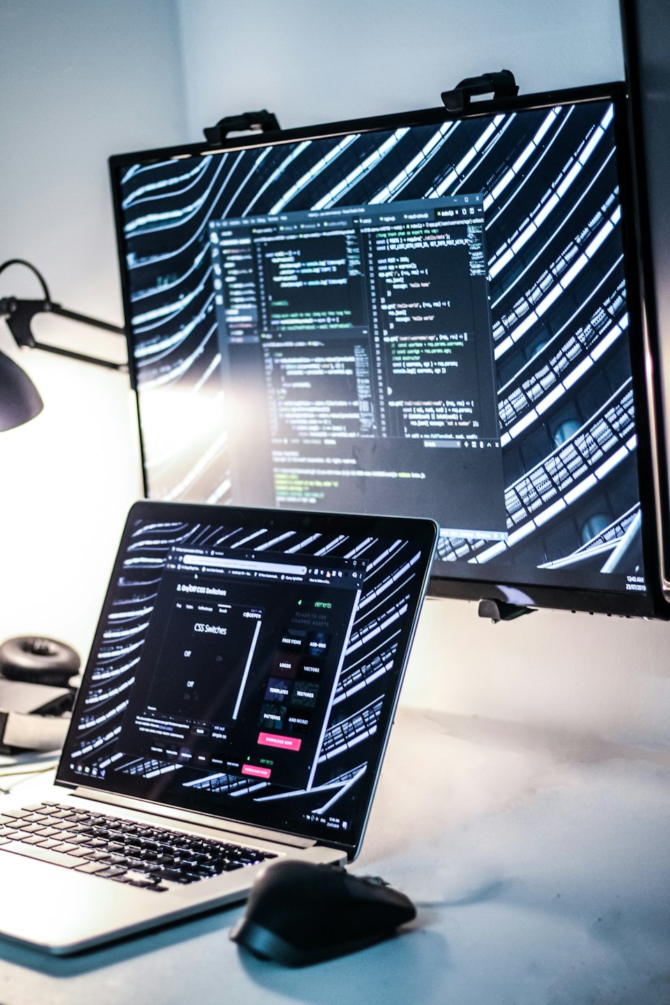 Laptop dan monitor menampilkan kode di kantor modern.