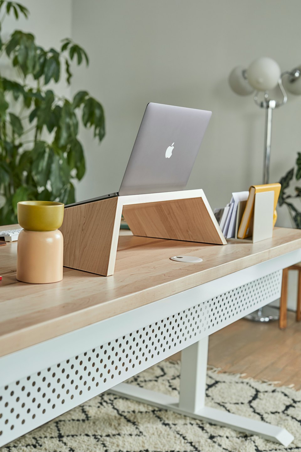 Laptop di atas dudukan kayu terang di atas meja modern.